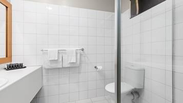 A modern bathroom with white tiles, a glass shower enclosure, a toilet, and a sink with a mirror.