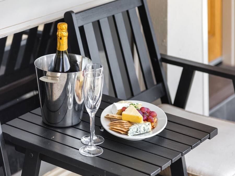 A table with a bottle of champagne, two glasses, and a plate of cheese, crackers, and grapes.