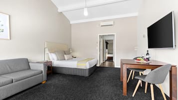 Een hotelkamer met een bed, een grijze bank, een houten eettafel met twee stoelen en een flatscreen televisie.