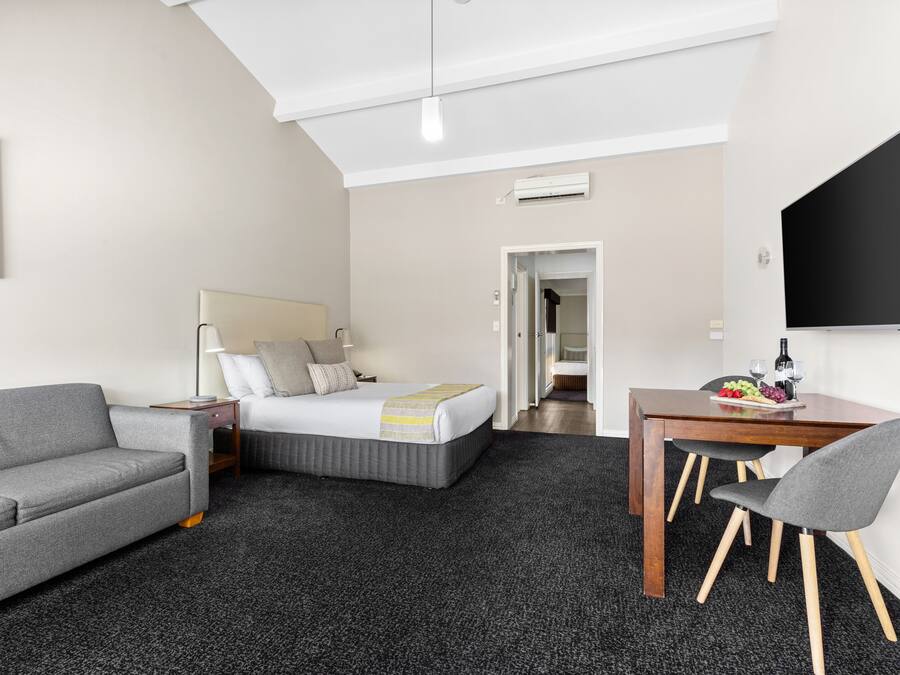 Een hotelkamer met een bed, een grijze bank, een houten eettafel met twee stoelen en een flatscreen televisie.