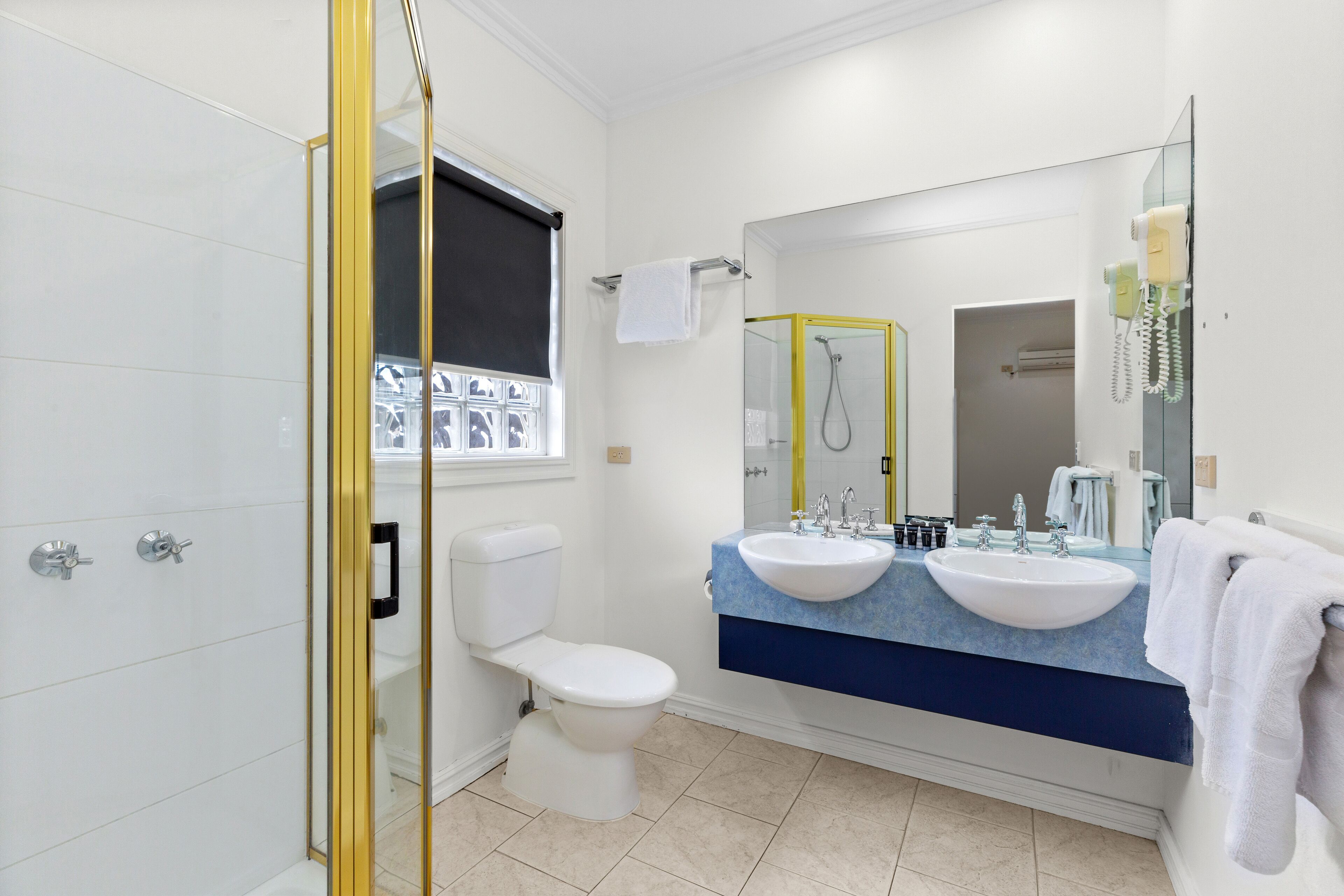 A modern bathroom with a toilet, bidet, and shower. It features a large mirror, dual sinks, and a vanity with a towel rack.