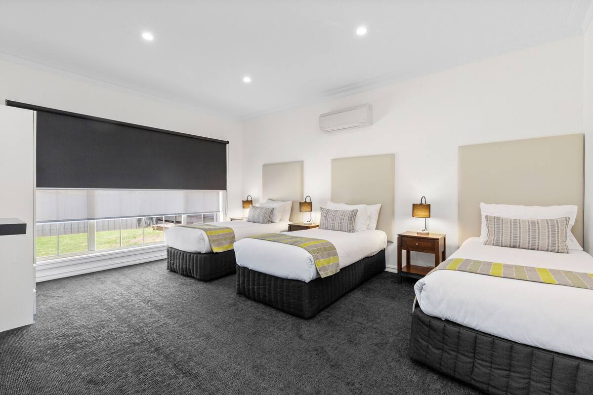Quarto de hotel com três camas, uma janela grande com vista e uma varanda.