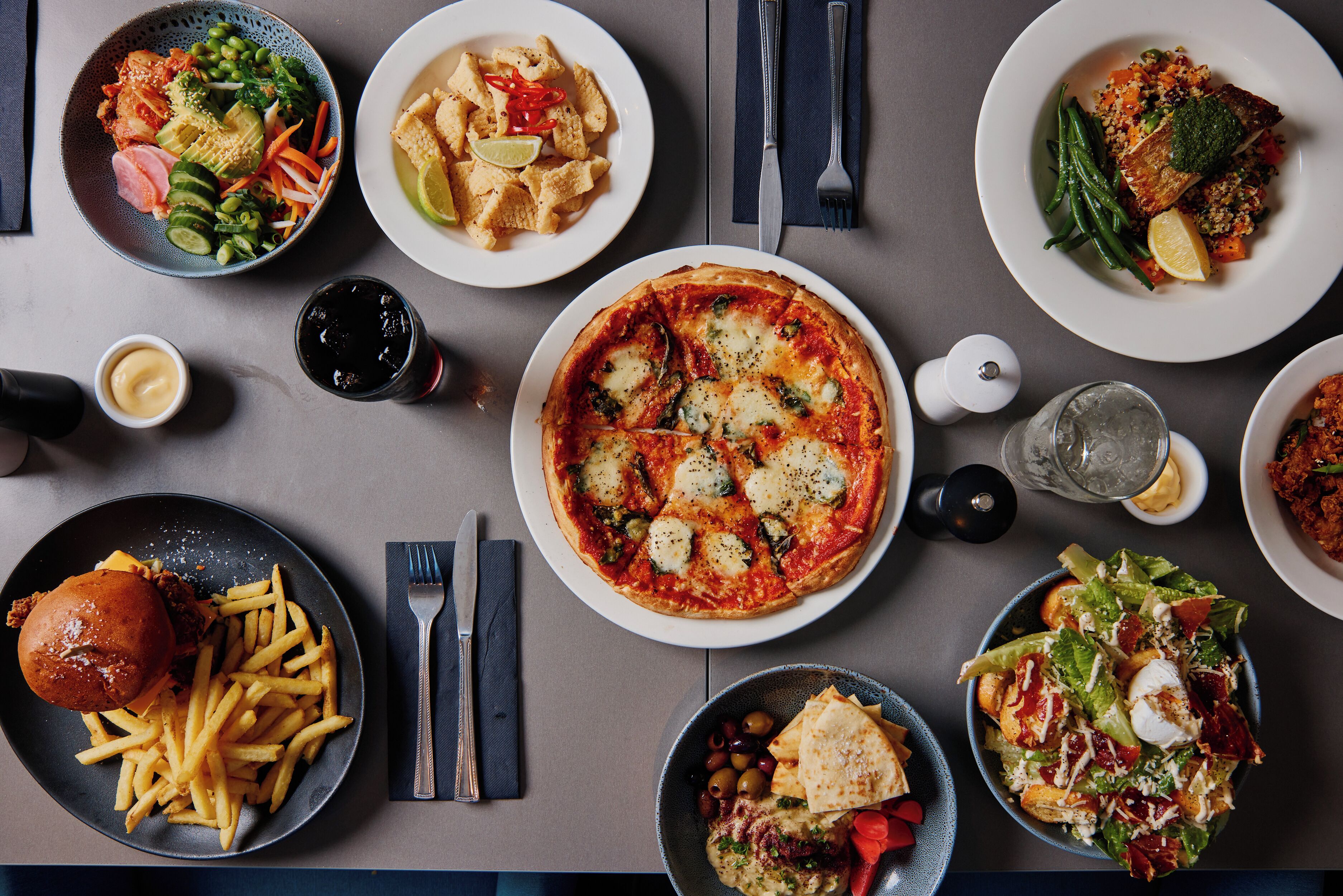Een tafel met diverse gerechten, waaronder pizza, salade en een hamburger.