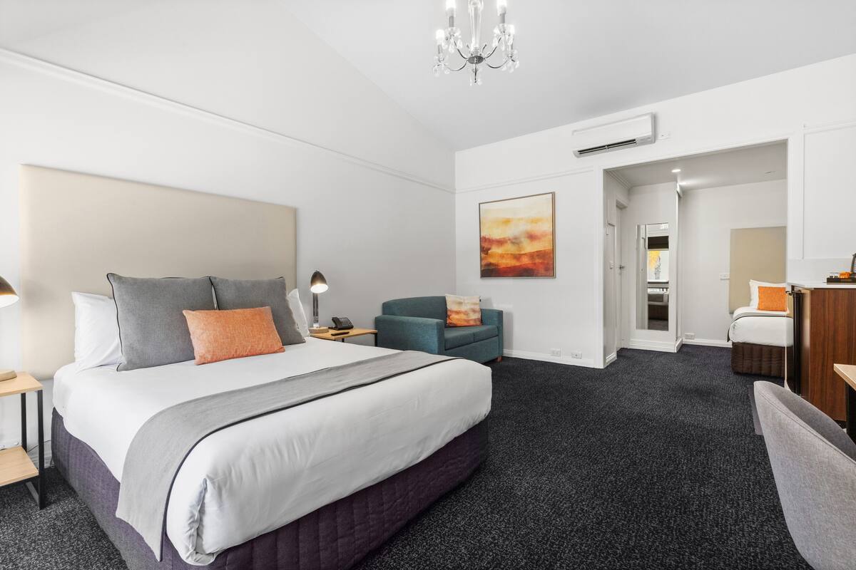 Quarto de hotel moderno com uma cama grande, uma escrivaninha, uma cadeira e um quadro na parede.