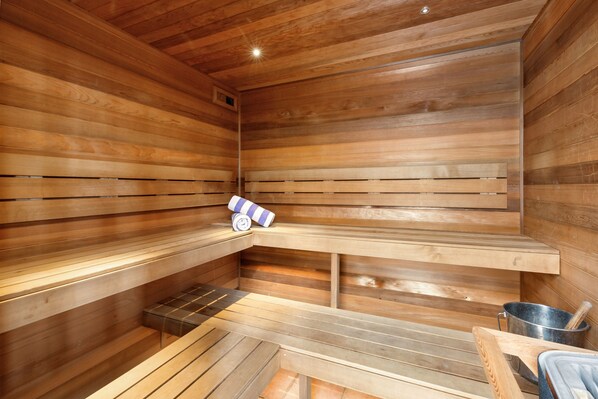 A sauna with wooden benches, a bench heater, and a metal container. - All Seasons Resort (Strathdale)