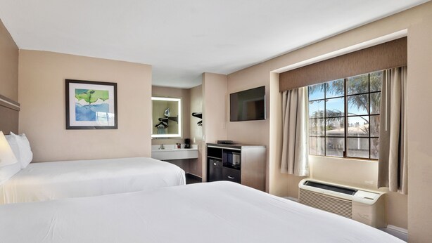 A hotel room with two beds, a desk, a TV, and a window with curtains. - Executive Inn Hotel (Milpitas)