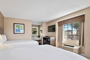 A hotel room with two beds, a desk, a TV, and a window with curtains.