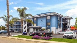 A multi-story building with a blue and white exterior, parking in front, and palm trees. - Executive Inn Hotel (Milpitas)