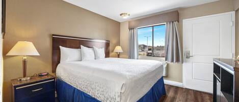 Una habitación de hotel con una cama grande, dos mesitas de noche con lámparas, un armario y vistas a la ciudad desde la ventana.