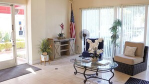 A hotel lobby with a glass coffee table, a sofa, a desk with a computer, an American flag, and a large window with blinds. - Country Inn (Ontario)