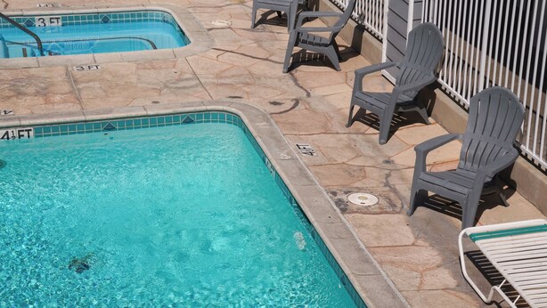 A swimming pool with a tiled edge, a 3 FT depth marker, and a 4 1/2 FT depth marker. There are several plastic chairs and a metal bench around the pool area. - Country Inn (Ontario)