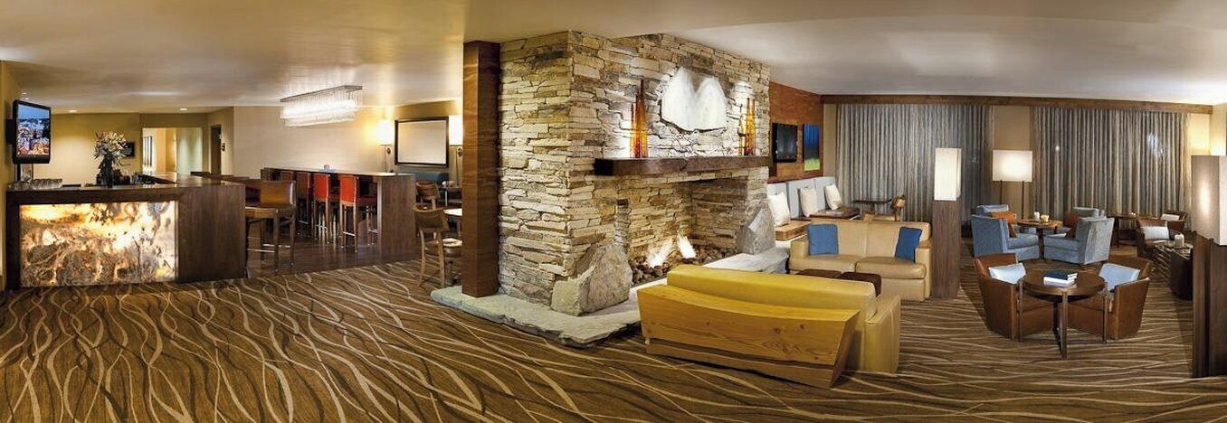 Vestíbulo de hotel con chimenea de piedra, zona de estar, bar y televisión.