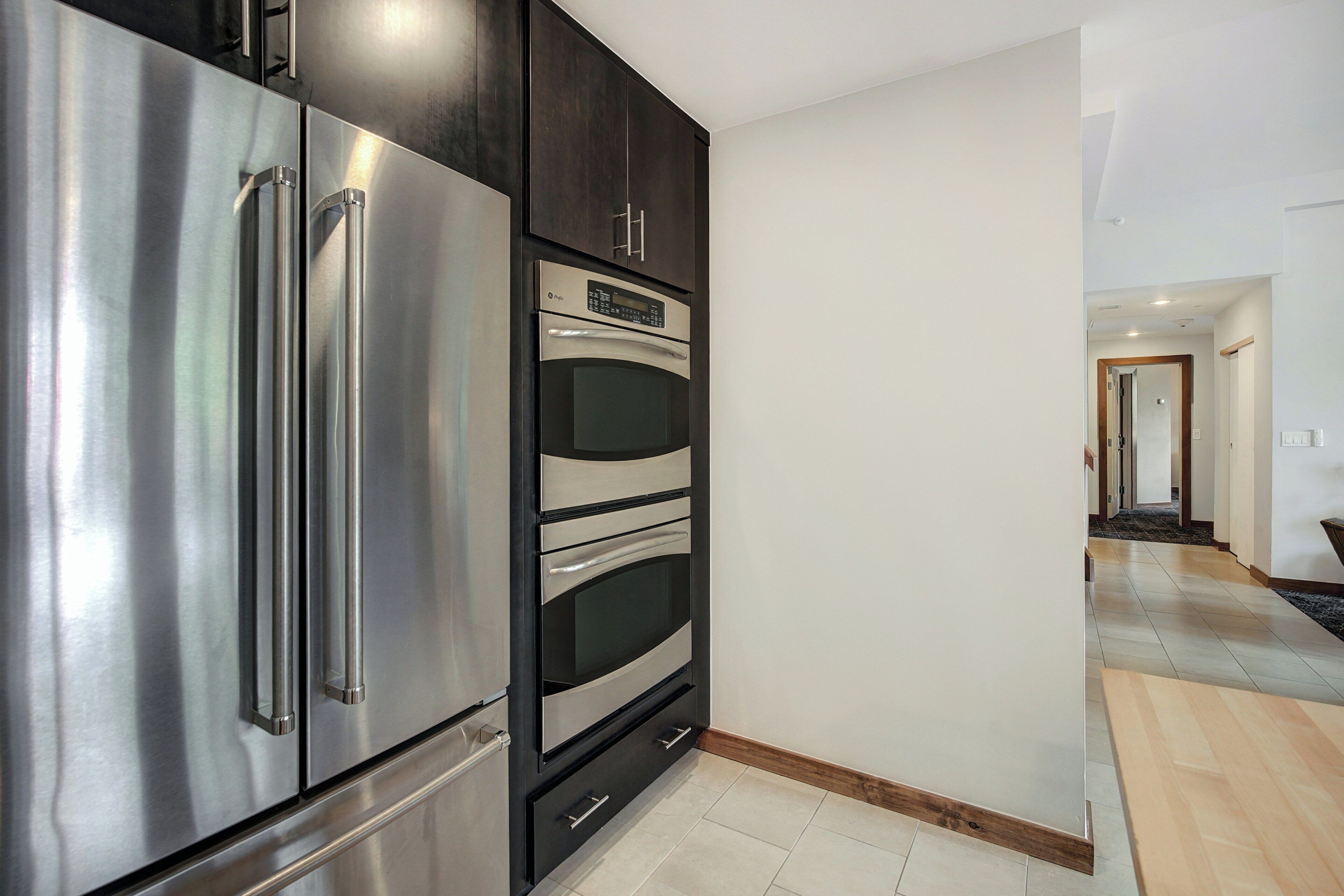 A modern kitchen with stainless steel appliances, a built-in oven, and a dark cabinetry design.