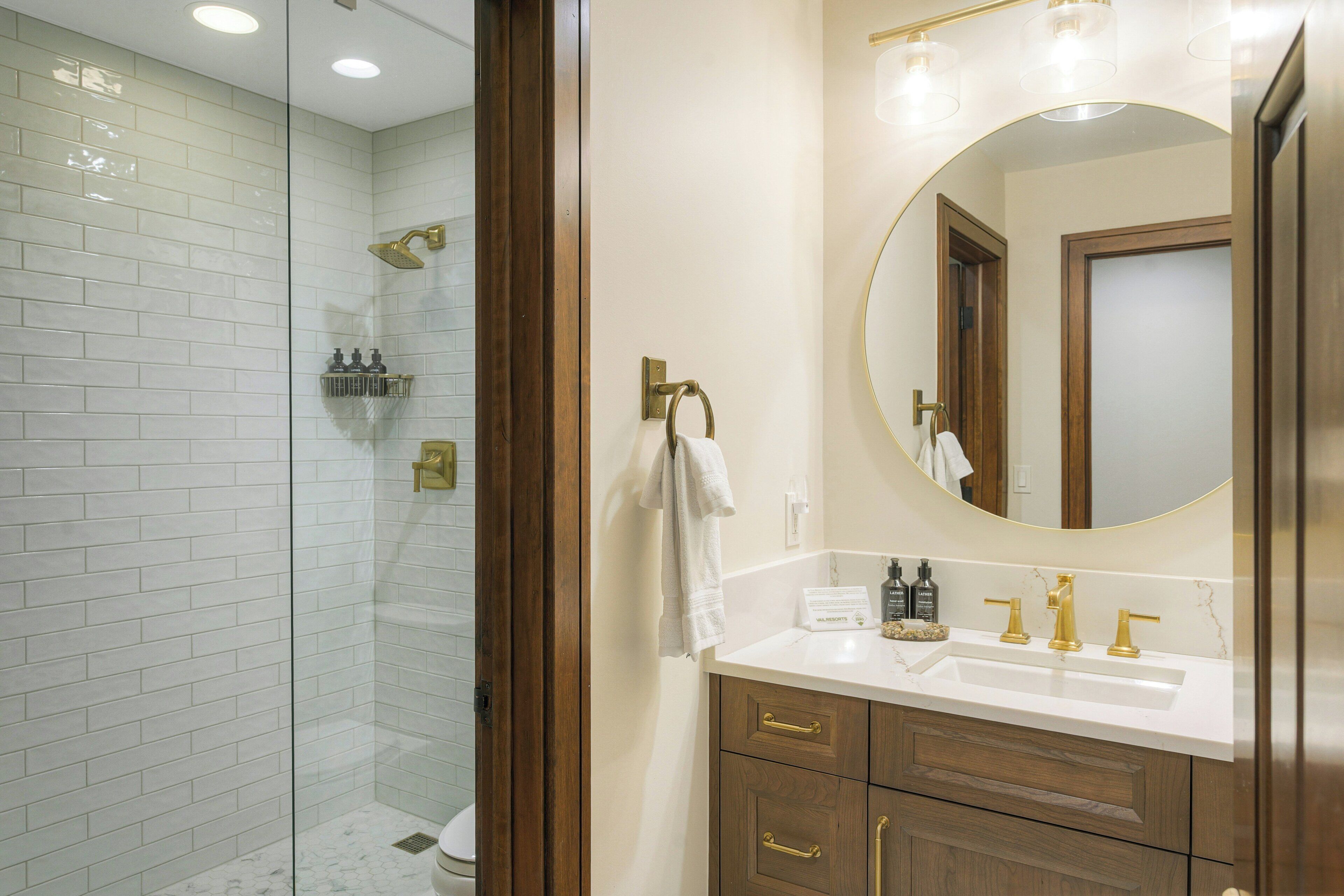 A bathroom with a glass-enclosed shower, a white sink with gold fixtures, and a wooden vanity.