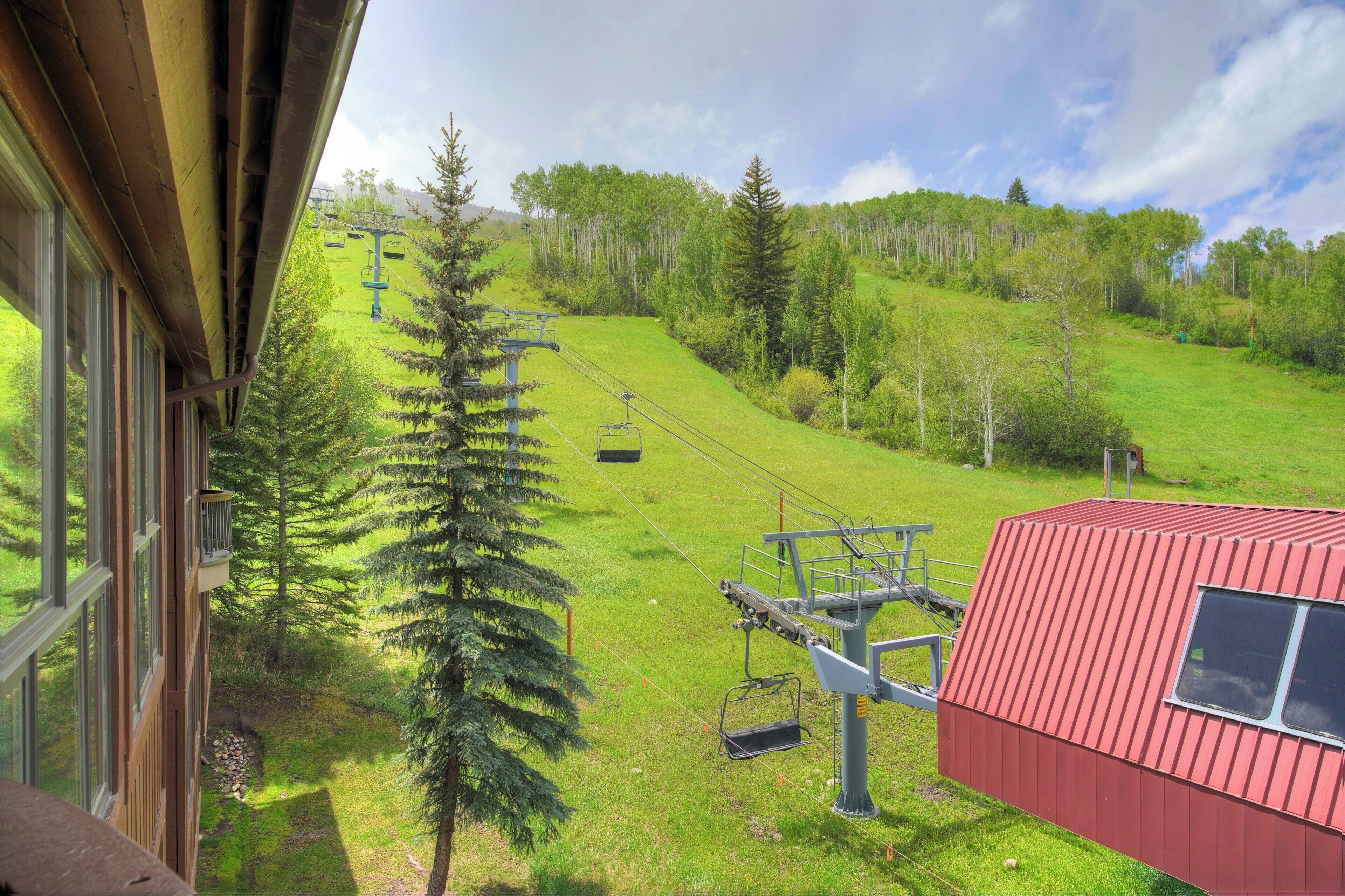 A ski lift, a red building, and a view of a green hillside with trees.