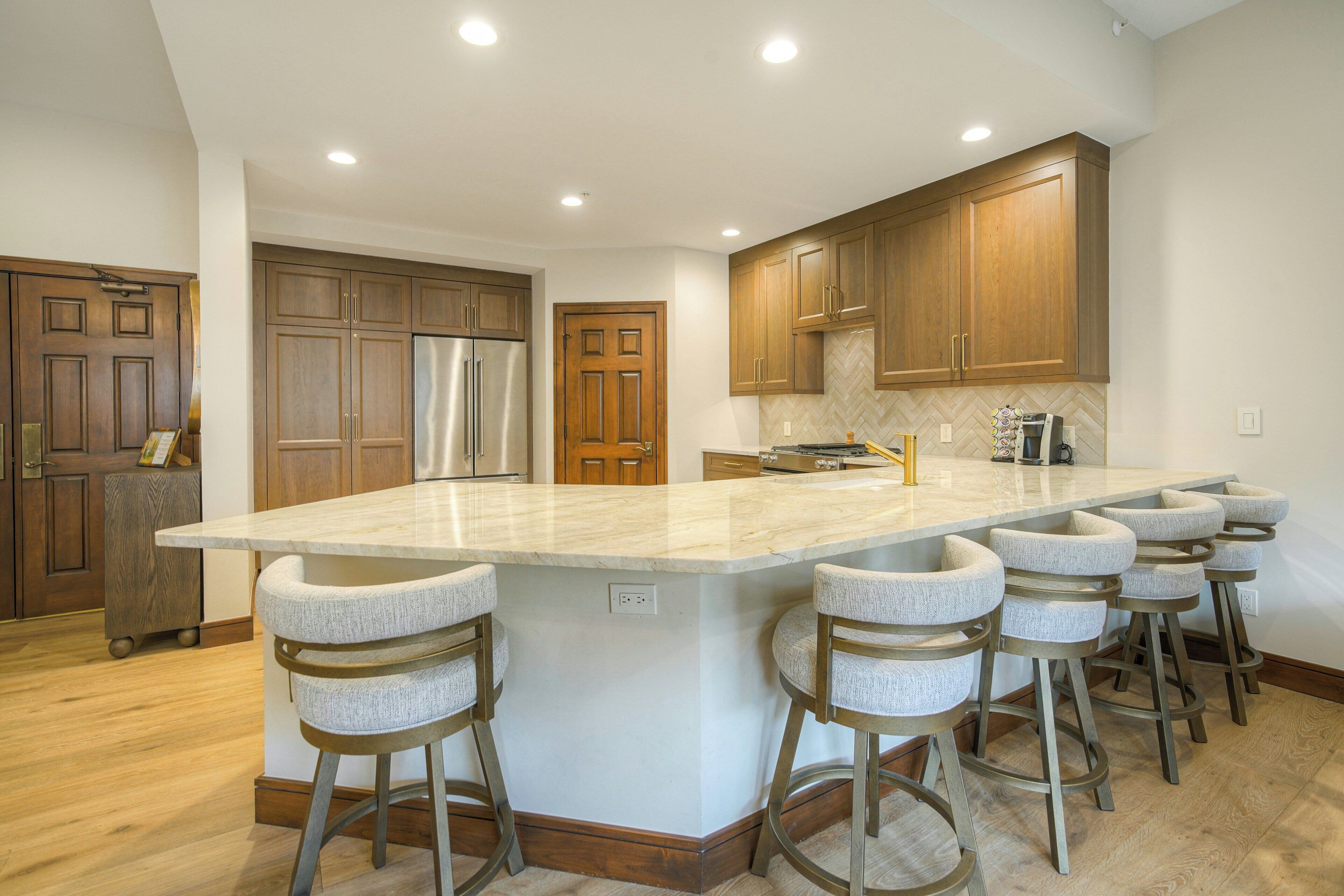 Una cocina moderna con una isla grande, armarios de madera, electrodomésticos de acero inoxidable y taburetes de bar.