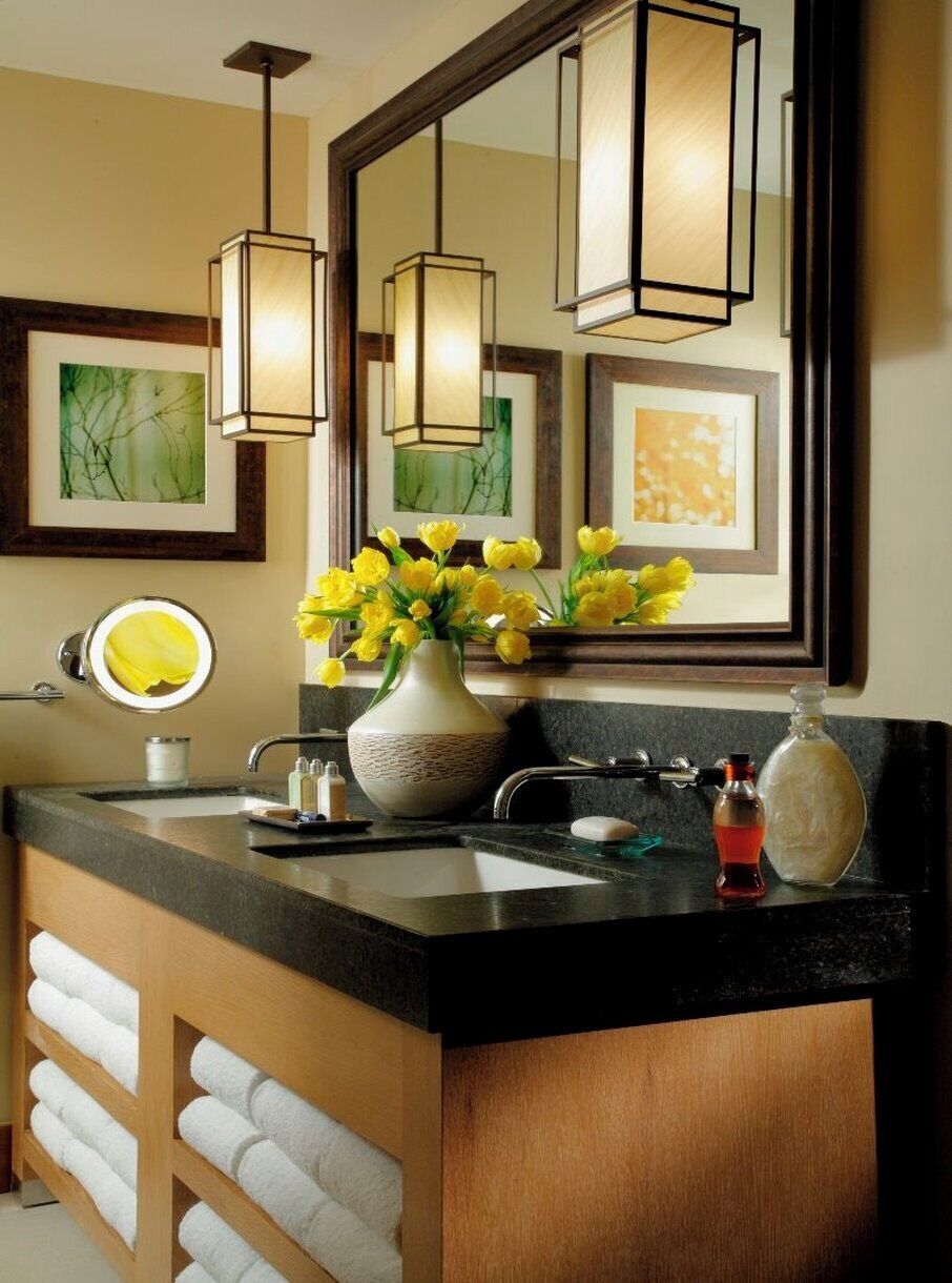 Une salle de bain avec un comptoir noir, un miroir, un vase avec des fleurs jaunes et un porte-serviettes.
