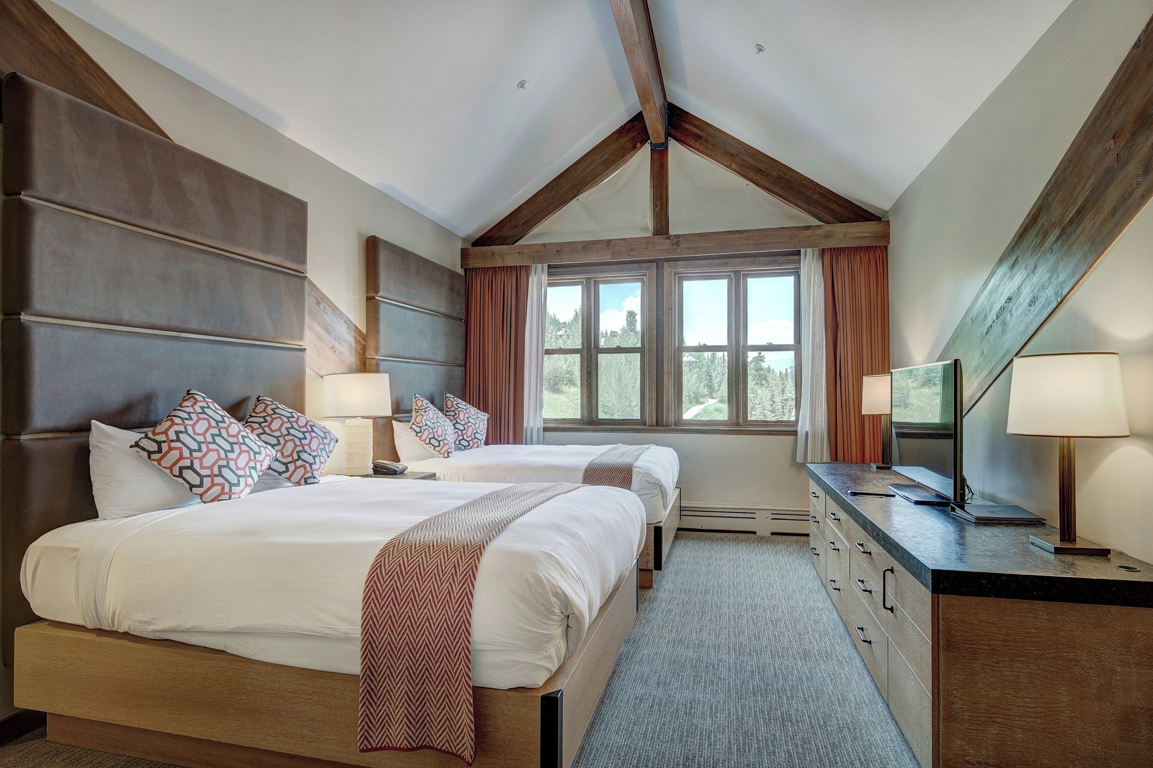 A bedroom with two beds, a dresser, a TV, and a window with curtains.
