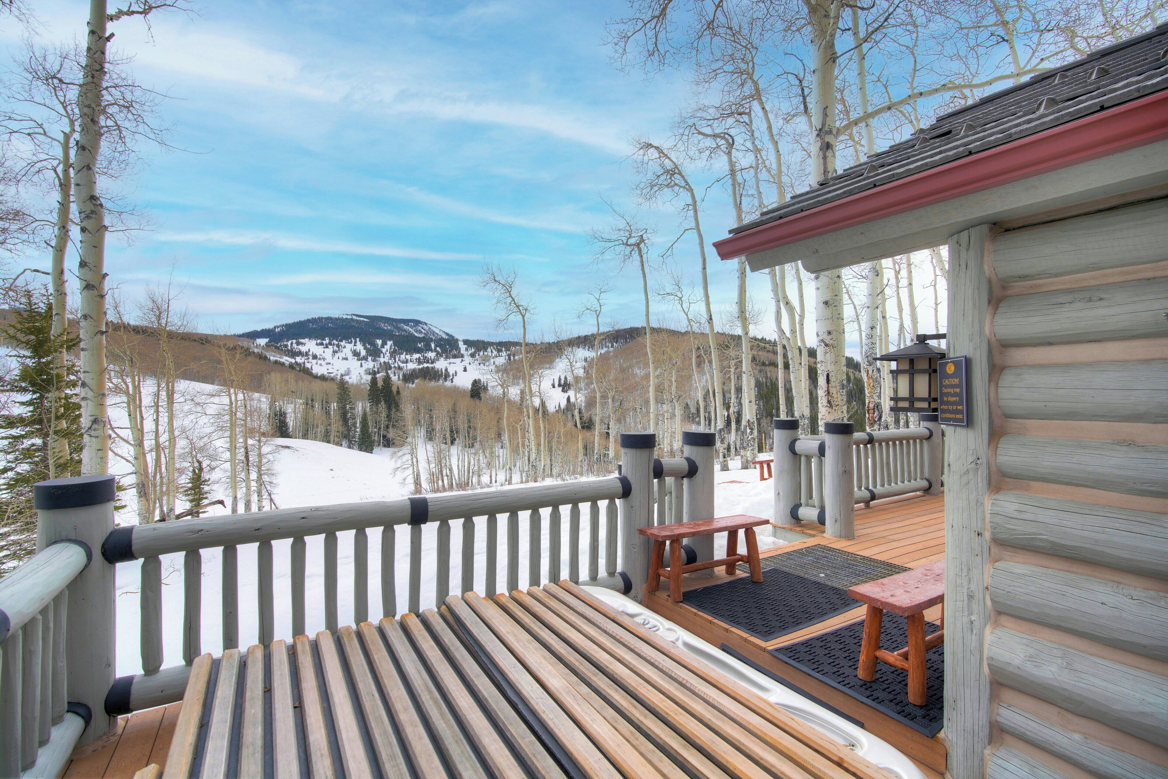 Una terraza de madera con un banco y una mesa, con vistas a un paisaje nevado con árboles y una montaña.