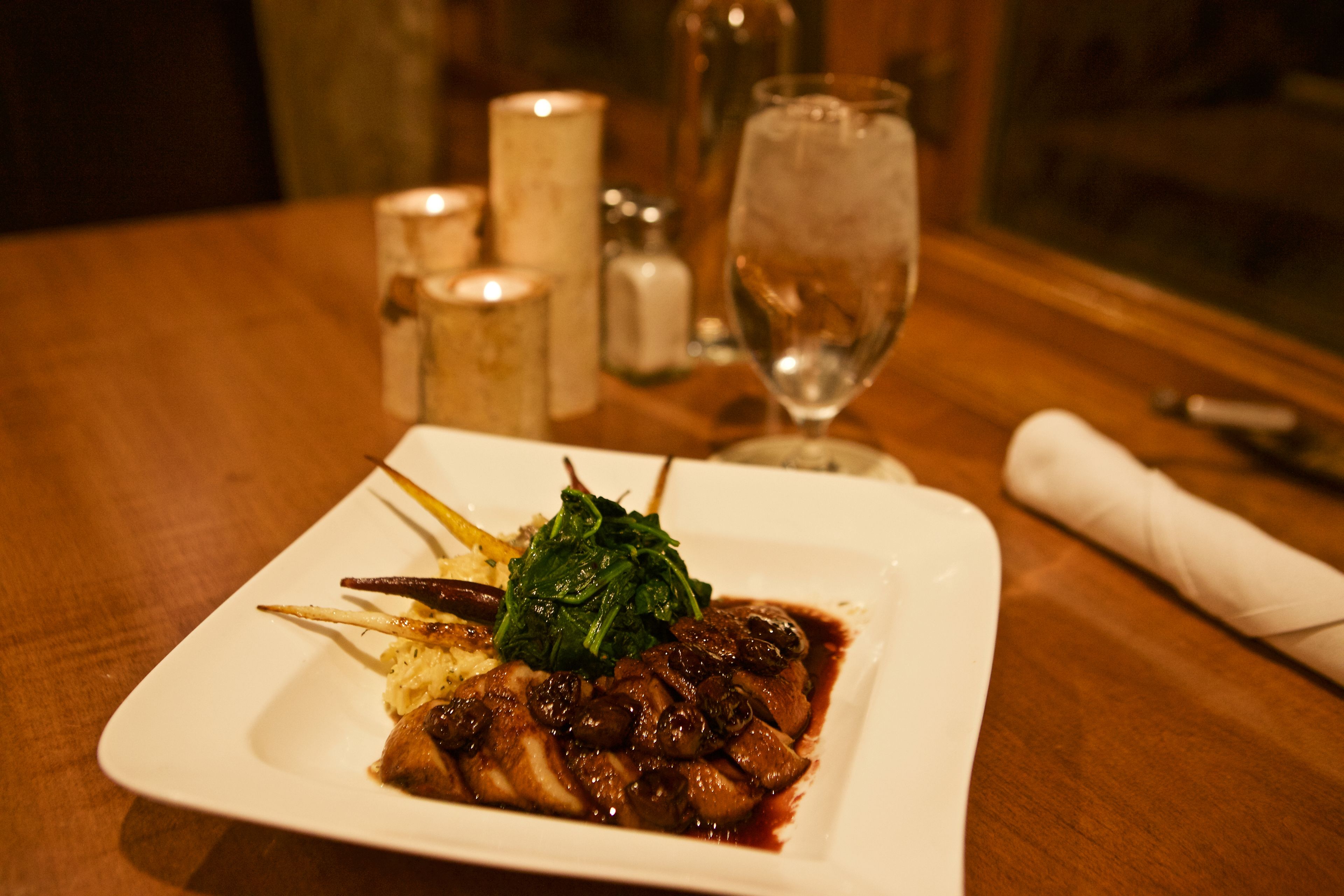 A square white plate with a dish of meat, greens, and a small portion of mashed potatoes.