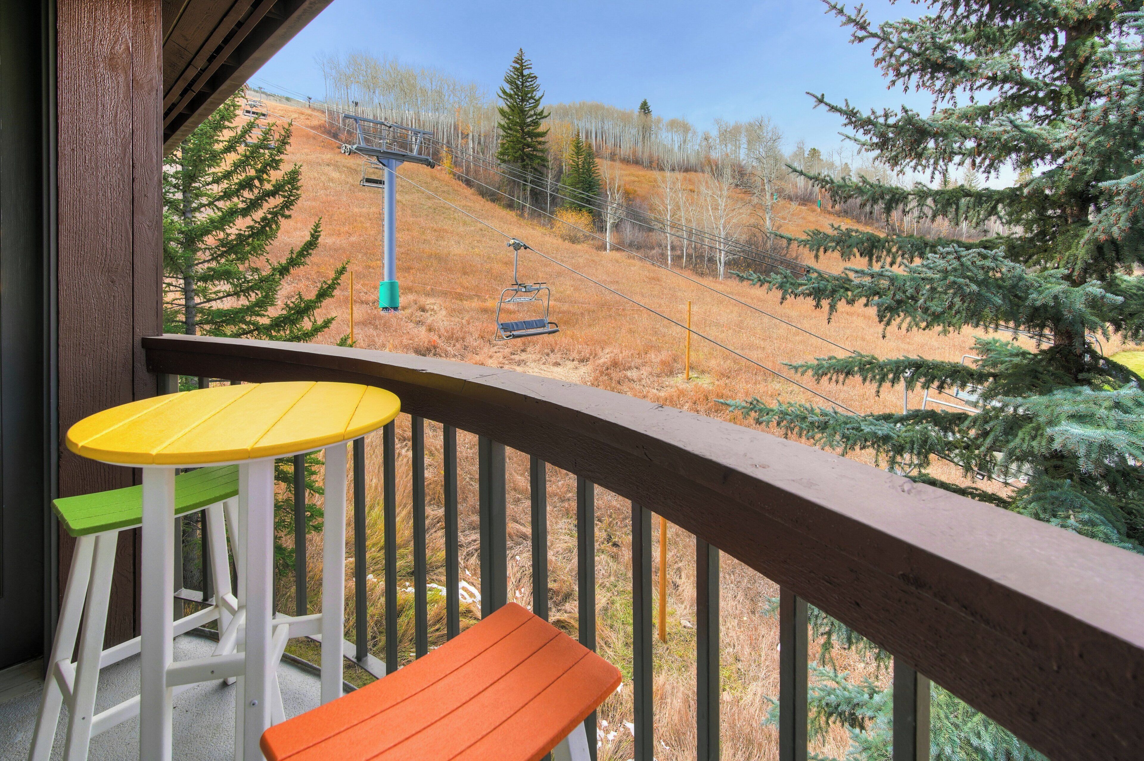 Un balcon avec une balustrade en bois, une table jaune et une chaise verte et orange.