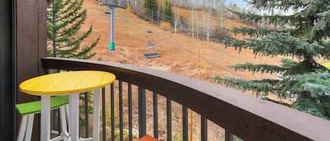 Un balcon avec une balustrade en bois, une table jaune et une chaise verte et orange.
