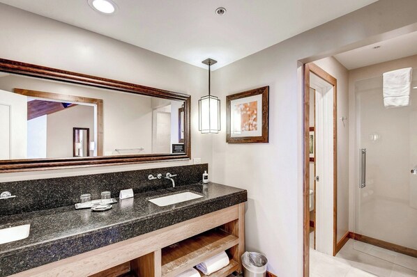 A modern bathroom with a granite countertop, a large mirror, a framed picture, and a walk-in shower. - The Osprey at Beaver Creek, a RockResort, by Vail Resorts (Avon)