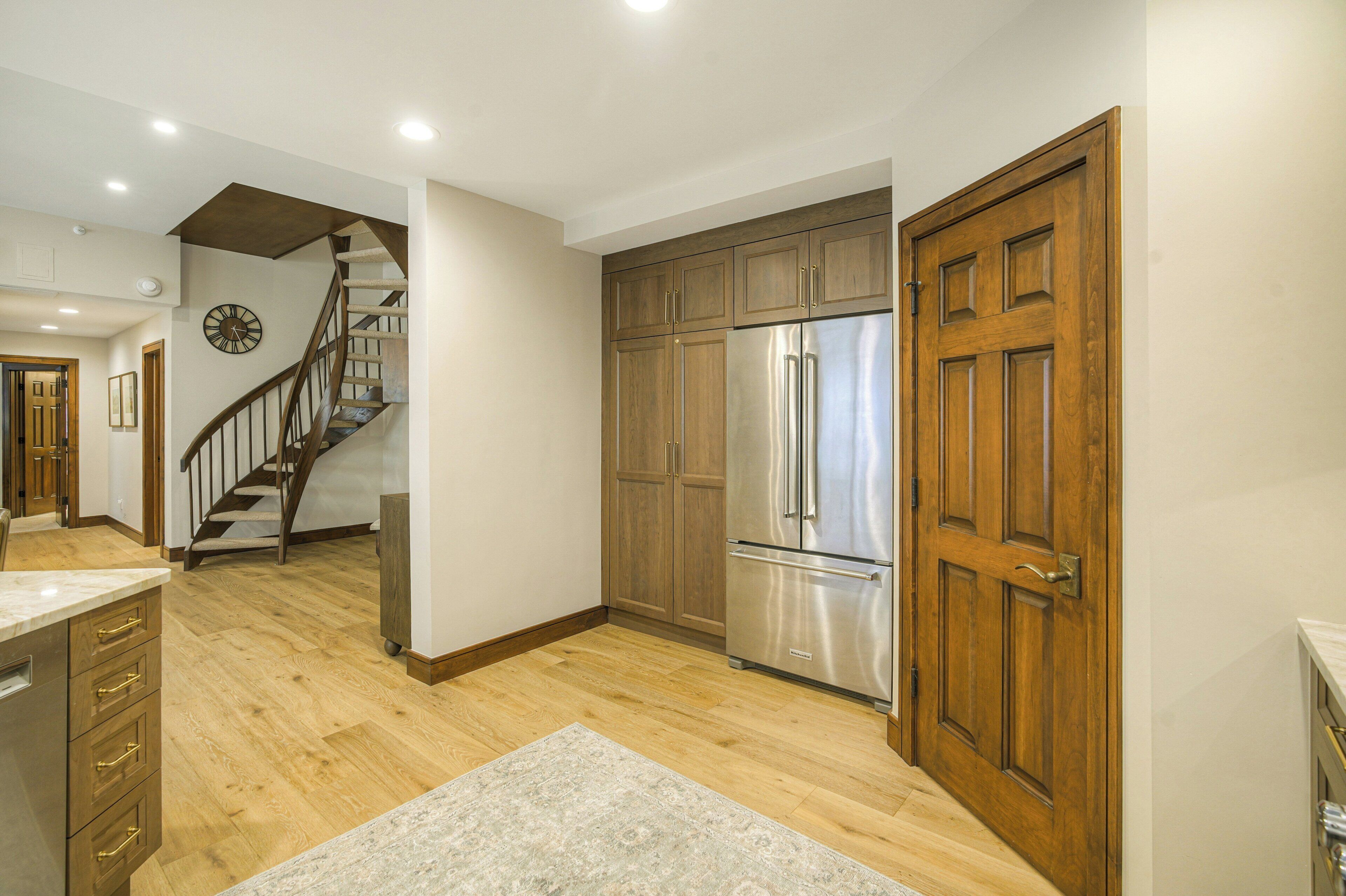 A modern kitchen with wooden cabinets, stainless steel appliances, and a wooden staircase.