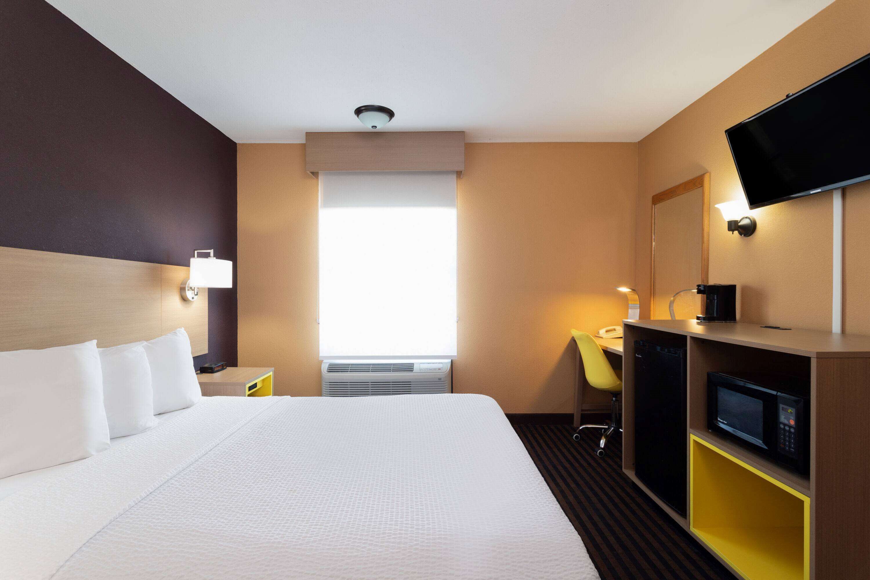 Hotellihuone, jossa on suuri sänky, työpöytä tuolilla, taulutelevisio ja mikroaaltouuni.