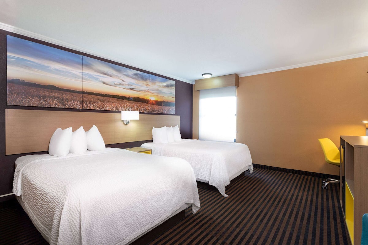 Una habitación de hotel con dos camas, un televisor grande montado en la pared, un escritorio y una silla.