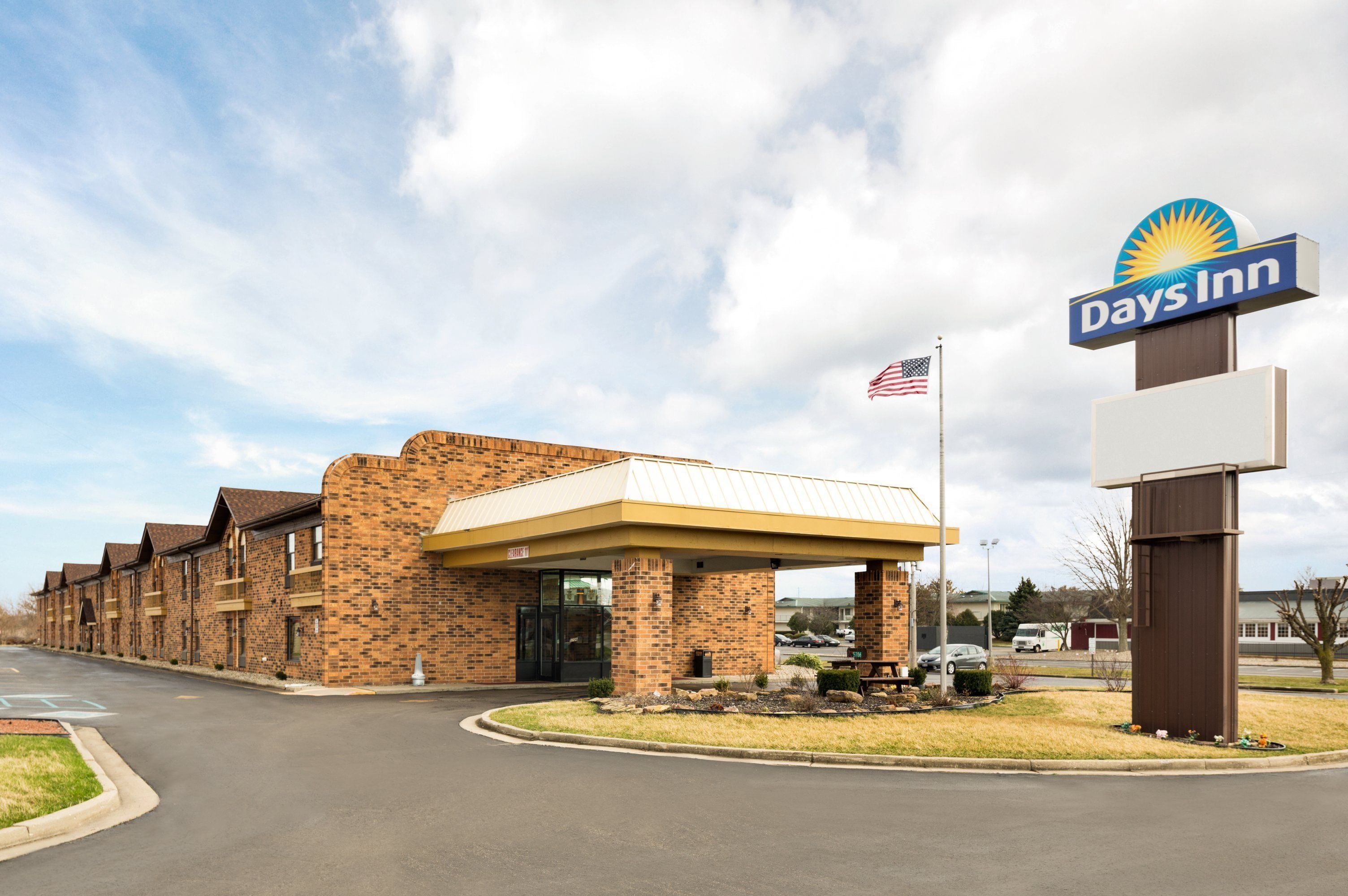 Un hôtel Days Inn avec une façade en briques, une entrée couverte et un drapeau américain.