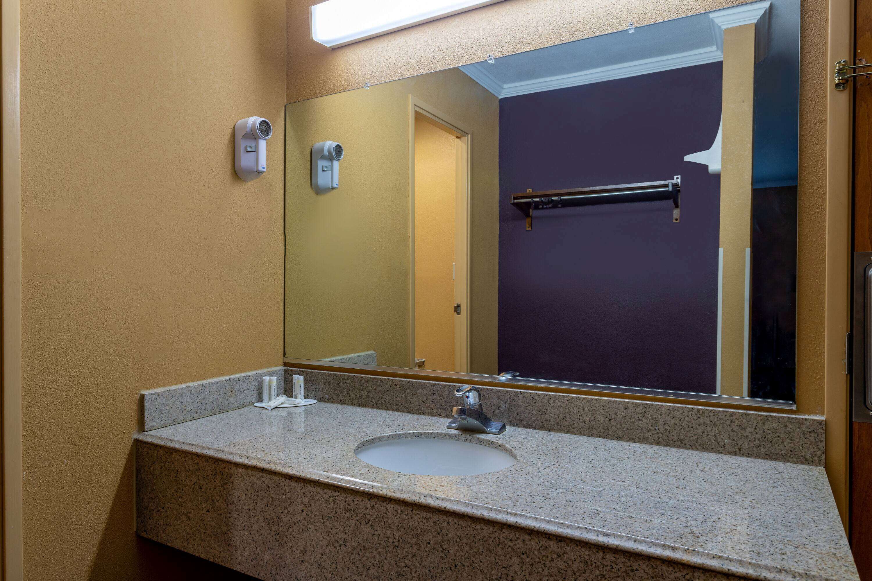 A bathroom with a granite countertop sink, a mirror, and a towel rack.