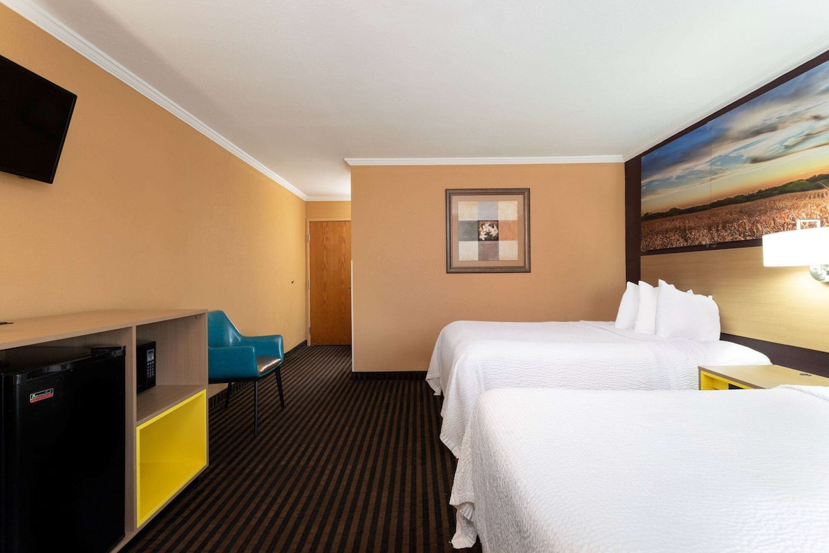 Habitación de hotel con dos camas, un escritorio con ordenador, televisor y un cuadro en la pared.