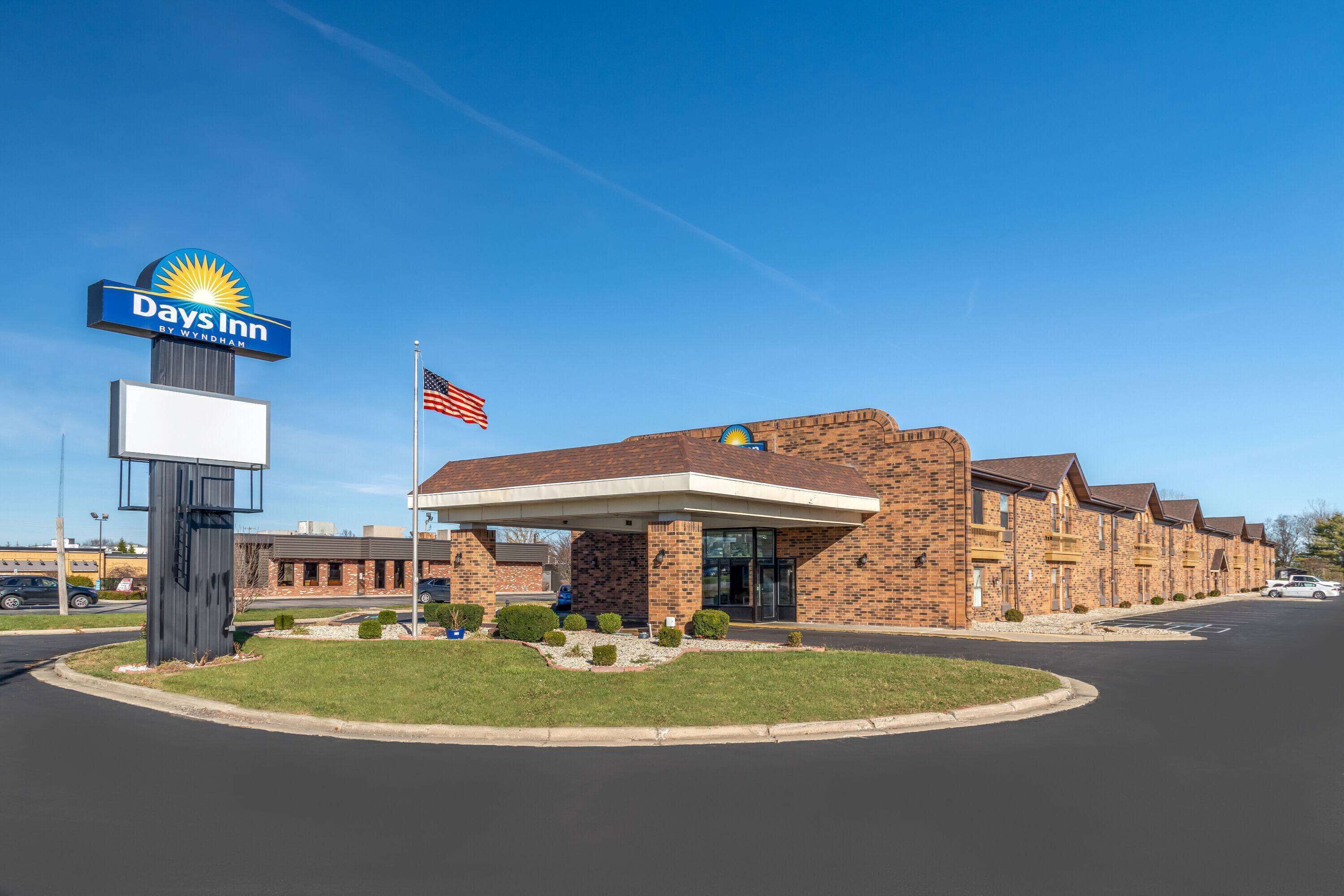 Um hotel Days Inn by Wyndham com fachada de tijolos, um posto de gasolina e uma bandeira americana.