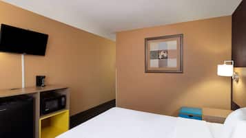 Habitación de hotel con cama, un televisor de pantalla plana en la pared, microondas, cafetera y un pequeño caja azul para guardar objetos.