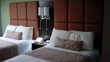A hotel room with two beds, each with white linens and beige pillows. There is a nightstand with a telephone and a lamp between the beds.