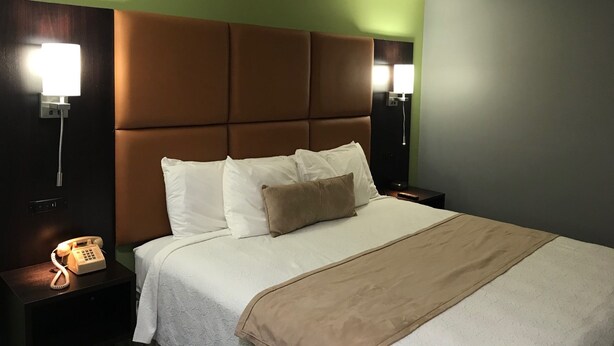 A hotel room with a large bed, a headboard, two bedside tables, a telephone, and wall-mounted lamps. - Inn at Portland (Portland)