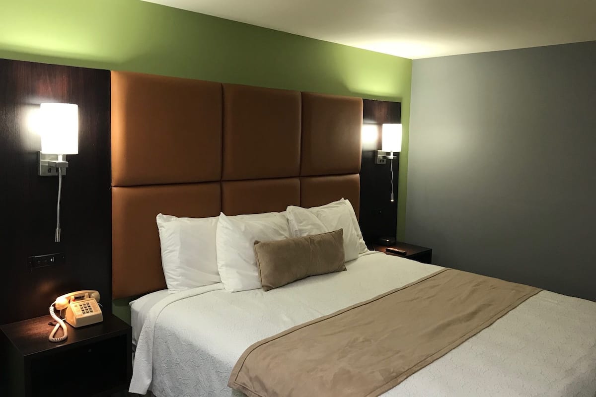 A hotel room with a large bed, a headboard, two bedside tables, a telephone, and wall-mounted lamps.