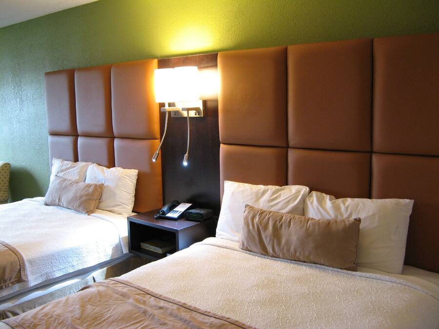 A hotel room with two beds, a nightstand with a phone, and a wall-mounted lamp.