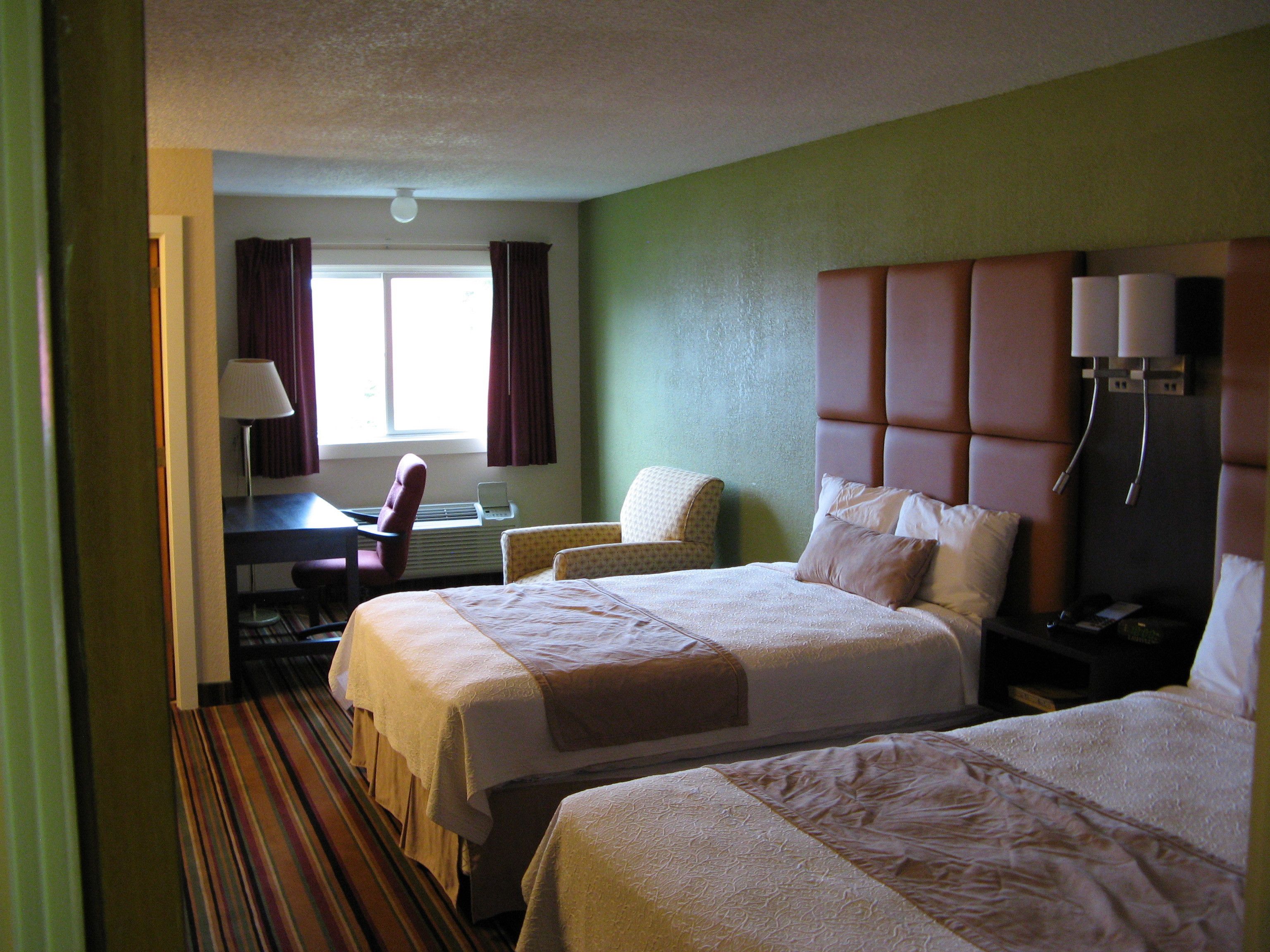 A hotel room with two beds, a desk, a chair, and a window with curtains.