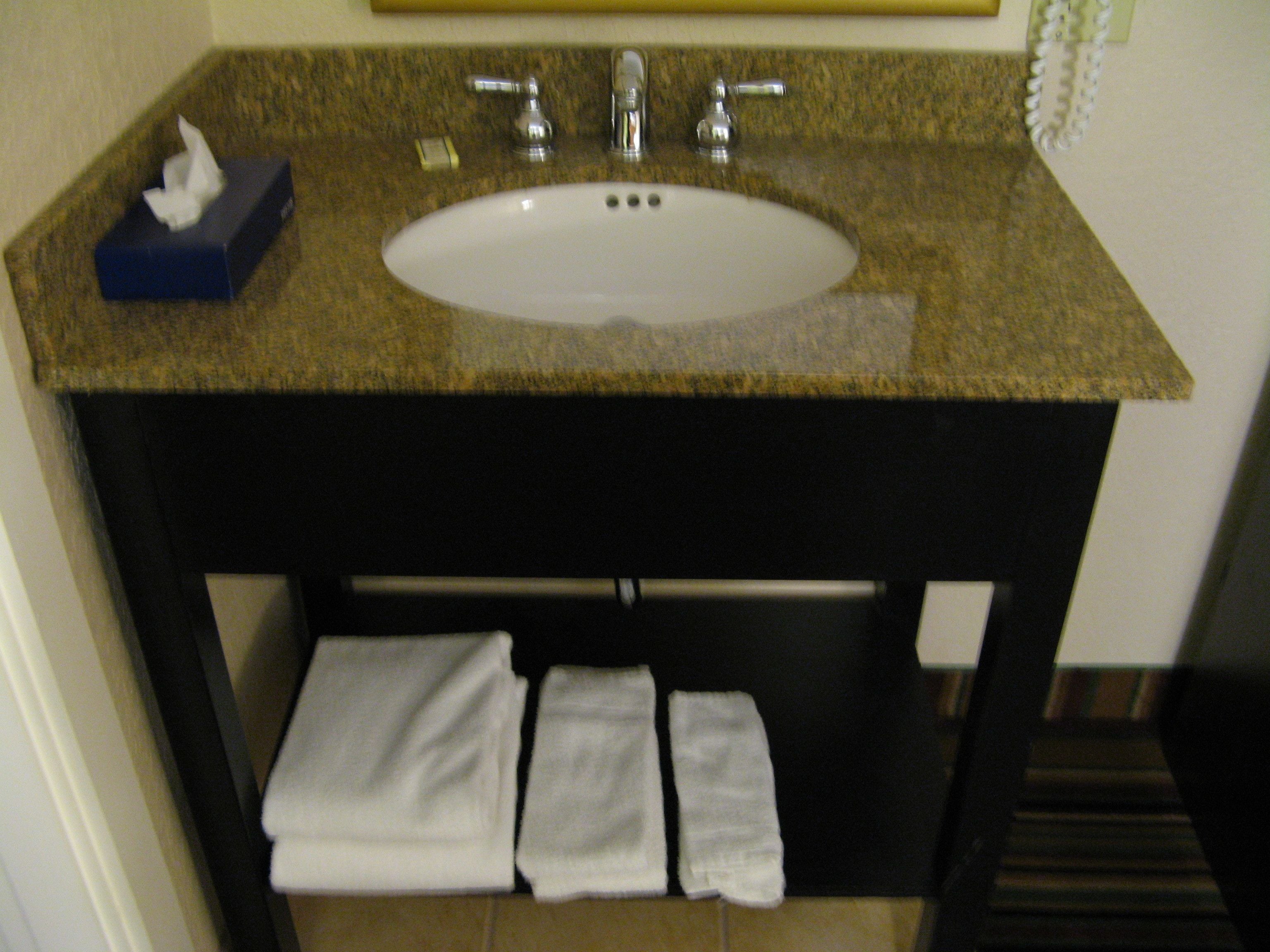 A bathroom with a granite countertop, a white sink, and a towel rack with three white towels.
