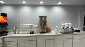 A breakfast bar with a coffee machine, cereal dispensers, and stacked white plates. - Inn at Portland (Portland)