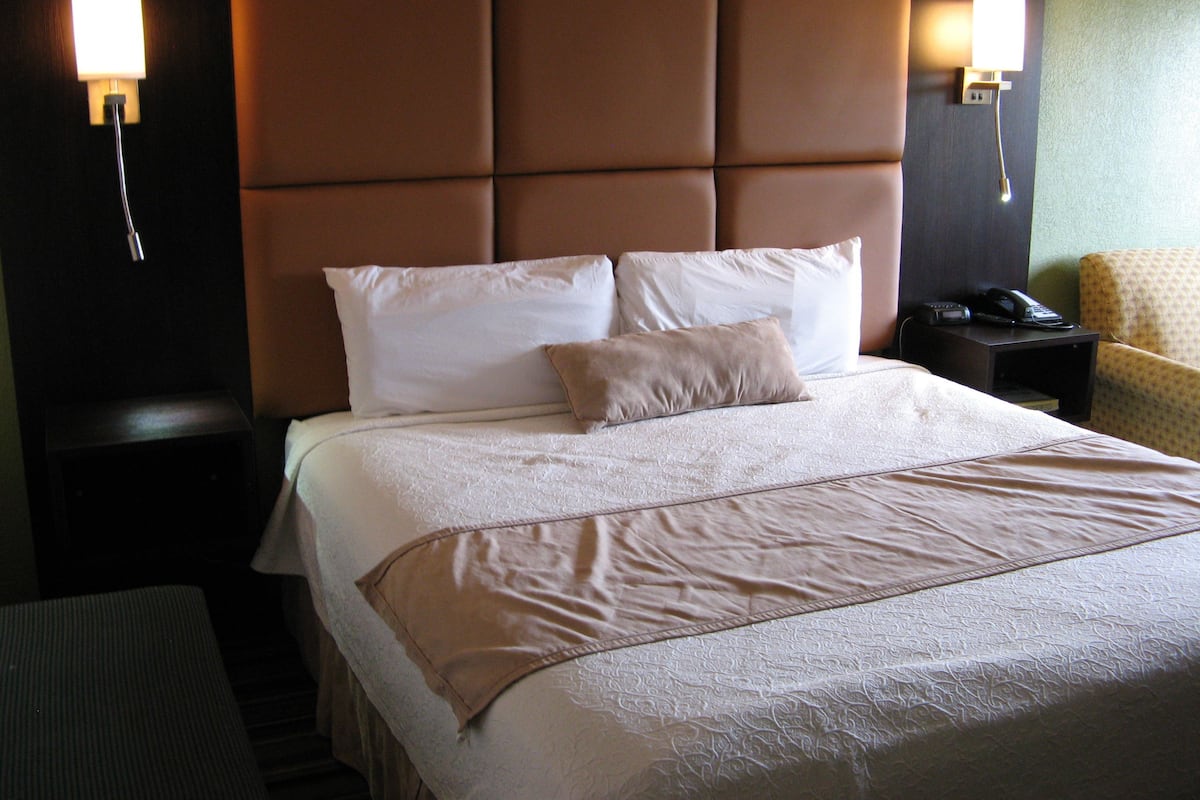 A hotel room with a large bed, two bedside tables, a chair, and a wall-mounted telephone.
