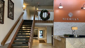 Eine Hotelhalle mit Treppe, einer Rezeption und einem Schild mit der Aufschrift 'Nichols'.