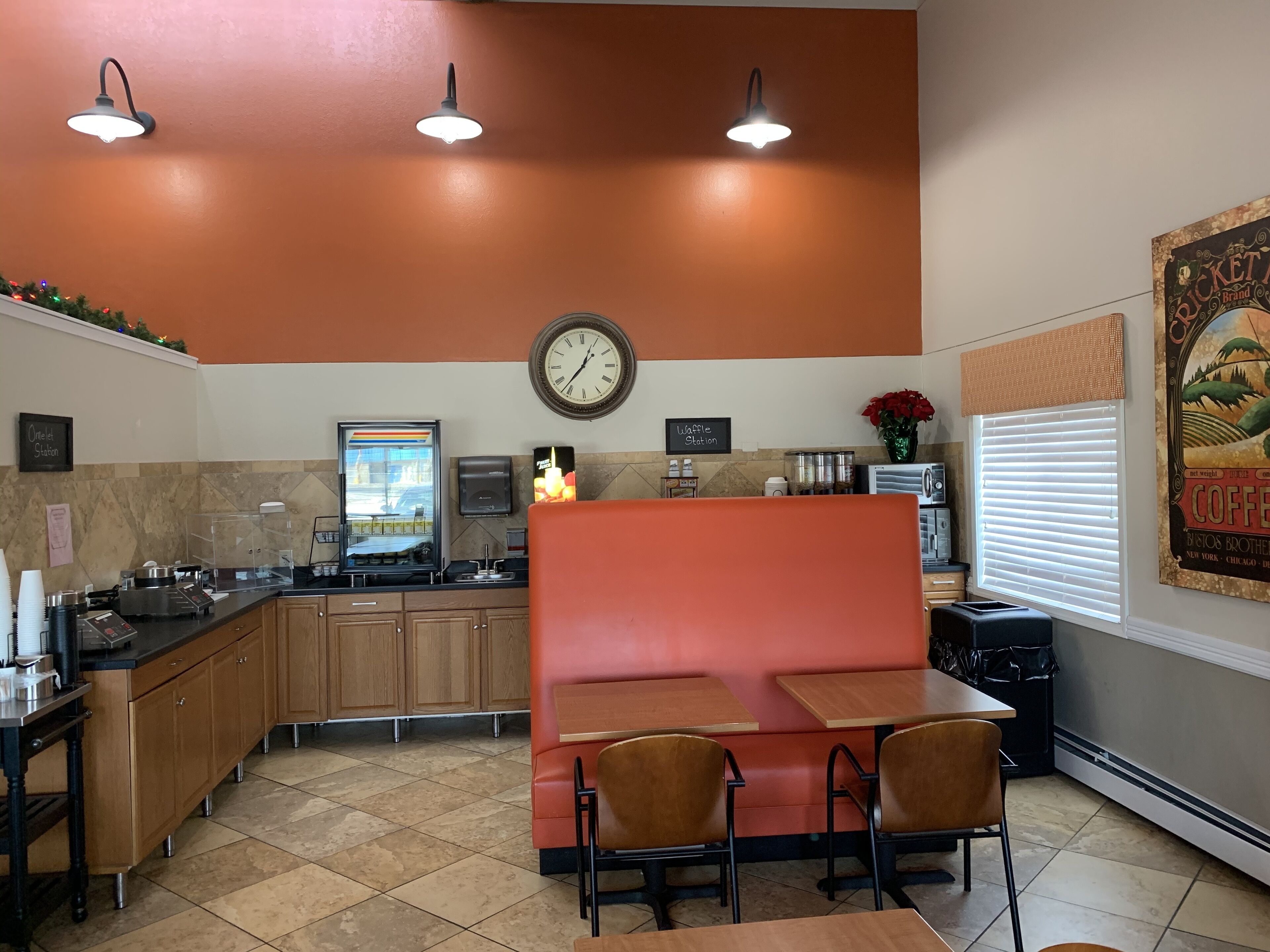 Un restaurante con un rincón de asientos en rojo tipo cabina, una estación de café y un reloj en la pared.