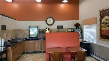Un restaurante con un rincón de asientos en rojo tipo cabina, una estación de café y un reloj en la pared.
