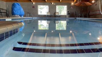 Una piscina interior con paredes de azulejos, vigas de techo de madera y vistas despejadas al exterior a través de ventanas.