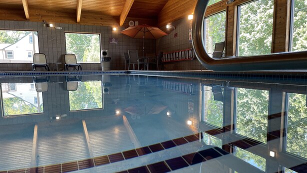 Ein Innenpool mit klaren Spiegelungen, Holzbalken an der Decke und großen Fenstern mit Blick auf Bäume.