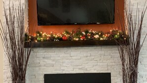 Ein Kamin mit darüber montiertem Fernseher, umgeben von dekorativem Grün und Ornamenten.