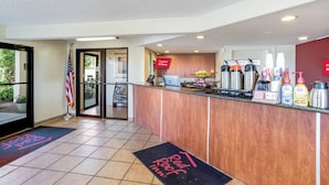 A hotel reception area with a wooden counter, a flag, a sign indicating free Wi-Fi, and a coffee station. - Red Roof Inn Gallup (Gallup)